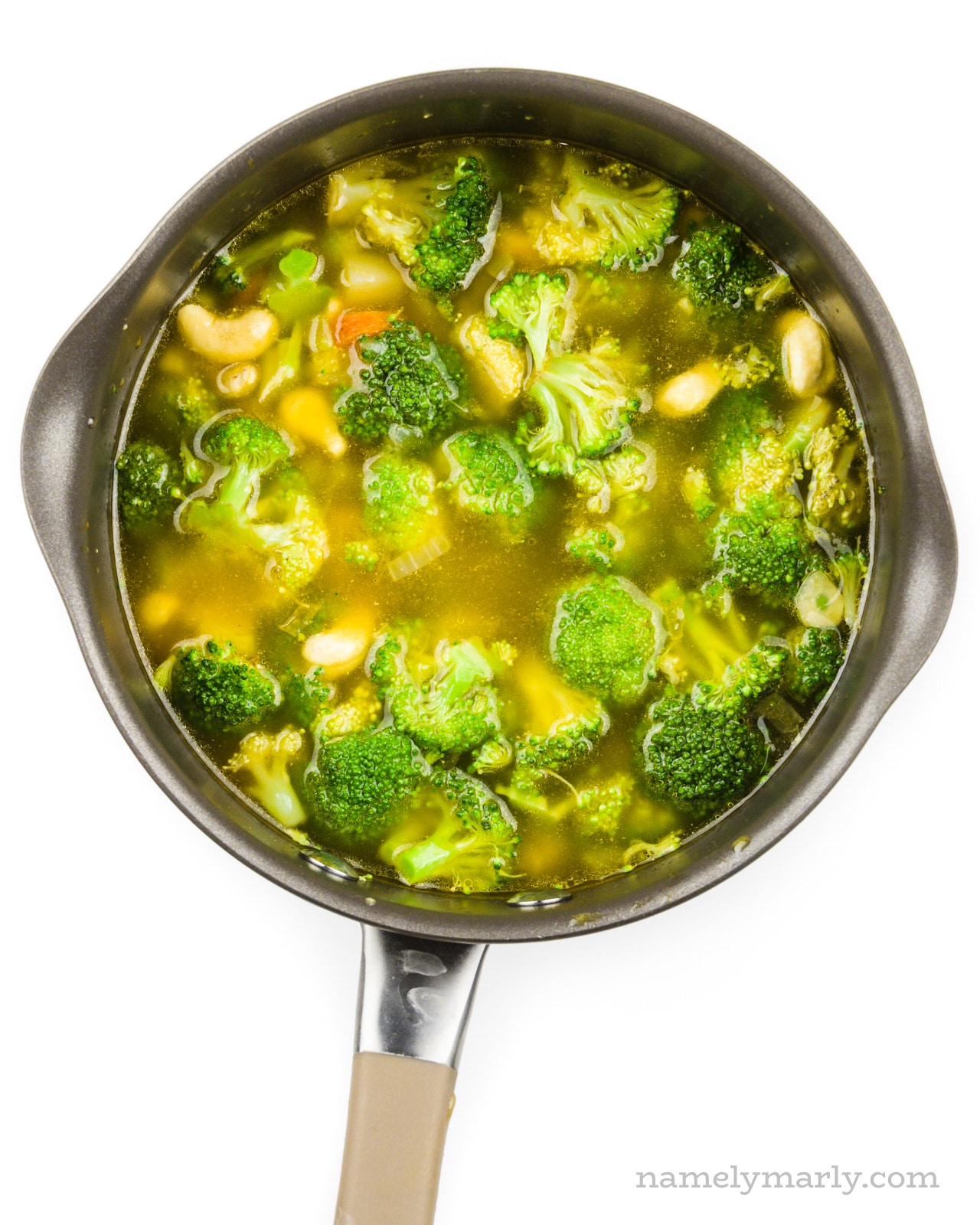 Looking down on a saucepan full of broth, cashews, broccoli, and other veggies.
