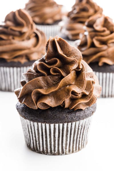 A group of cupcakes sit together, all with lots of chocolate frosting on top.