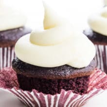 A closeup of a red velvet chocolate cupcake with lots of vegan cream cheese frosting on top!