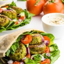 A pita is stuffed full of falafel, greens, chopped tomatoes and more to make a Falafel Sandwich. Other ingredients are behind it.