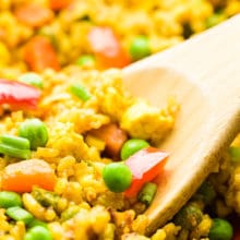 A closeup of a wood spoon in a skillet full of fried rice.