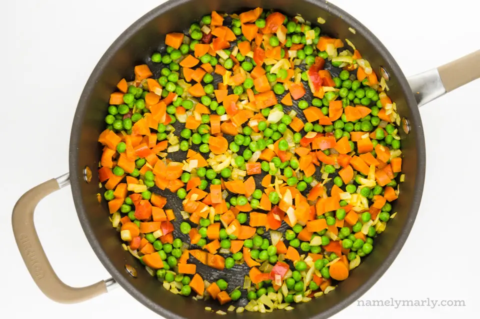 A skillet holds a mixture of vegetables, including peas, carrots, and red bell peppers.