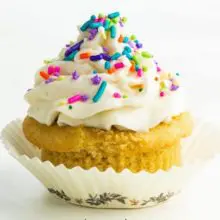 A vanilla cupcake is topped with vanilla frosting and colorful sprinkles.