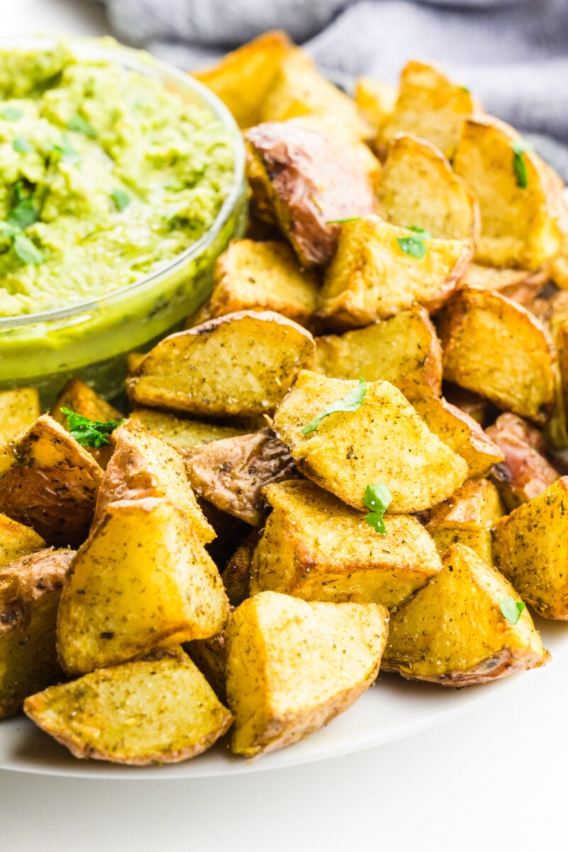 Air fryer potatoes sit next to a bowl of green sauce for dipping.