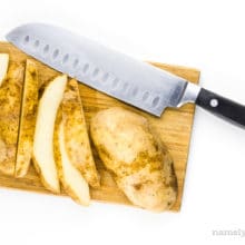 Cut up russet potatoes on a cutting board with a knife.