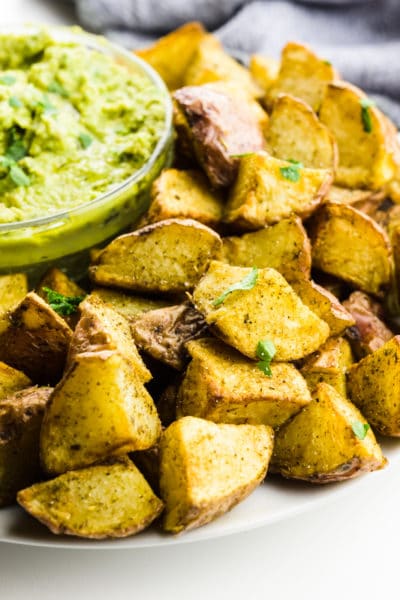 Air fryer potatoes sit next to a bowl of green sauce for dipping.