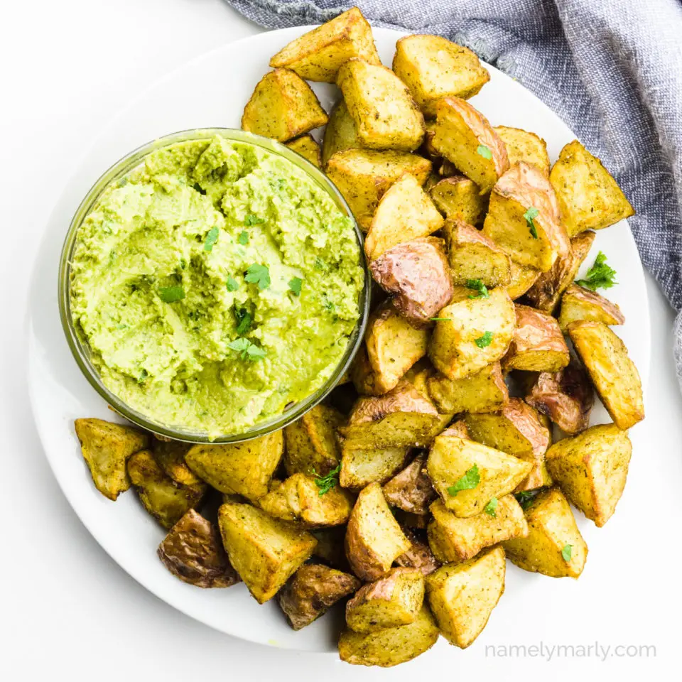 Looking down on a plate of air fryer potatoes with a bowl of green dipping sauce.