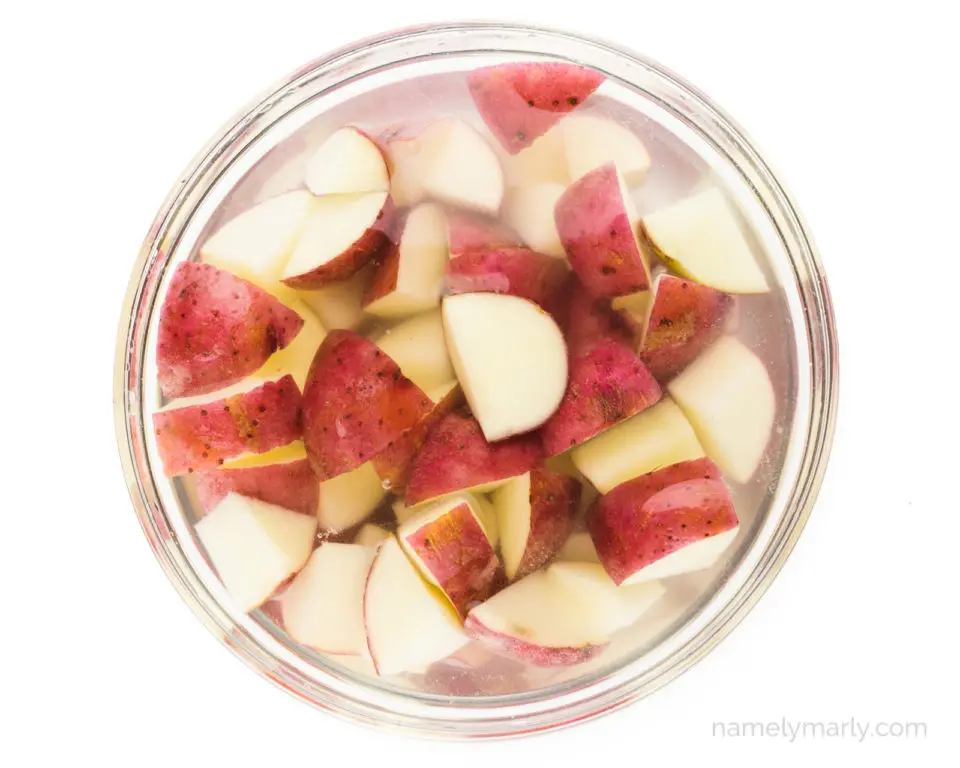 Cut red potatoes are soaking in a bowl of water.
