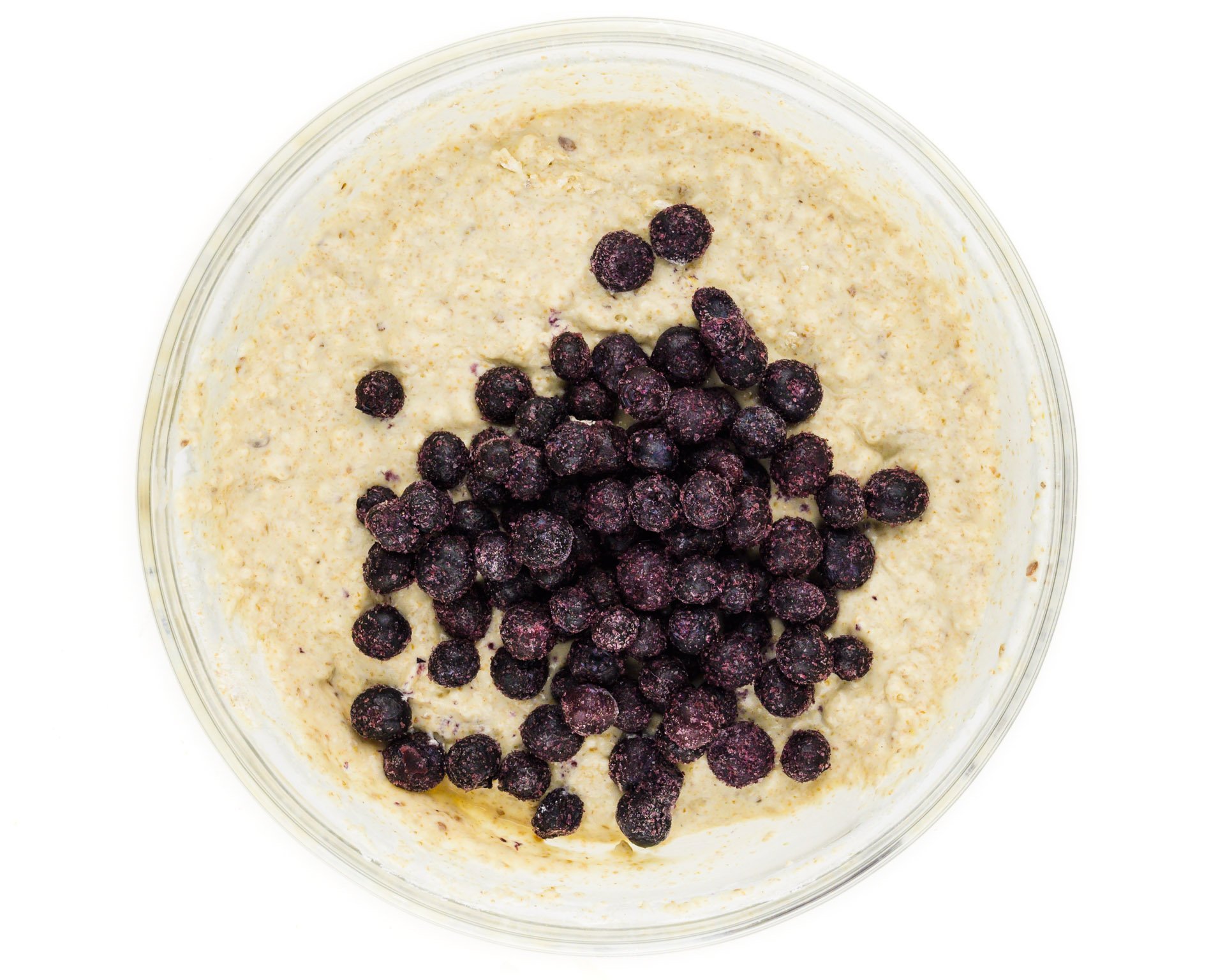 A bowl of waffle batter has frozen blueberries on top.