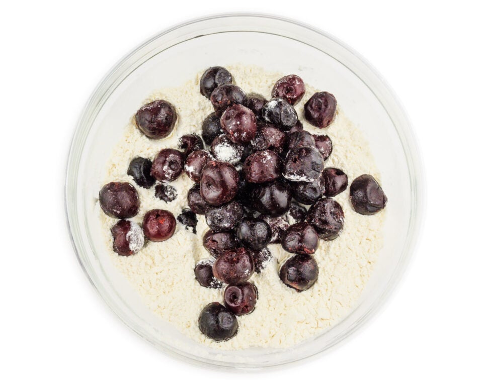 Frozen cherries are added to a bowl of flour.