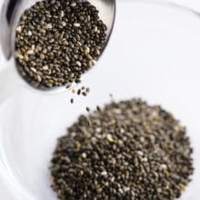 A tablespoon full of chia seeds is pouring them into a small glass bowl.