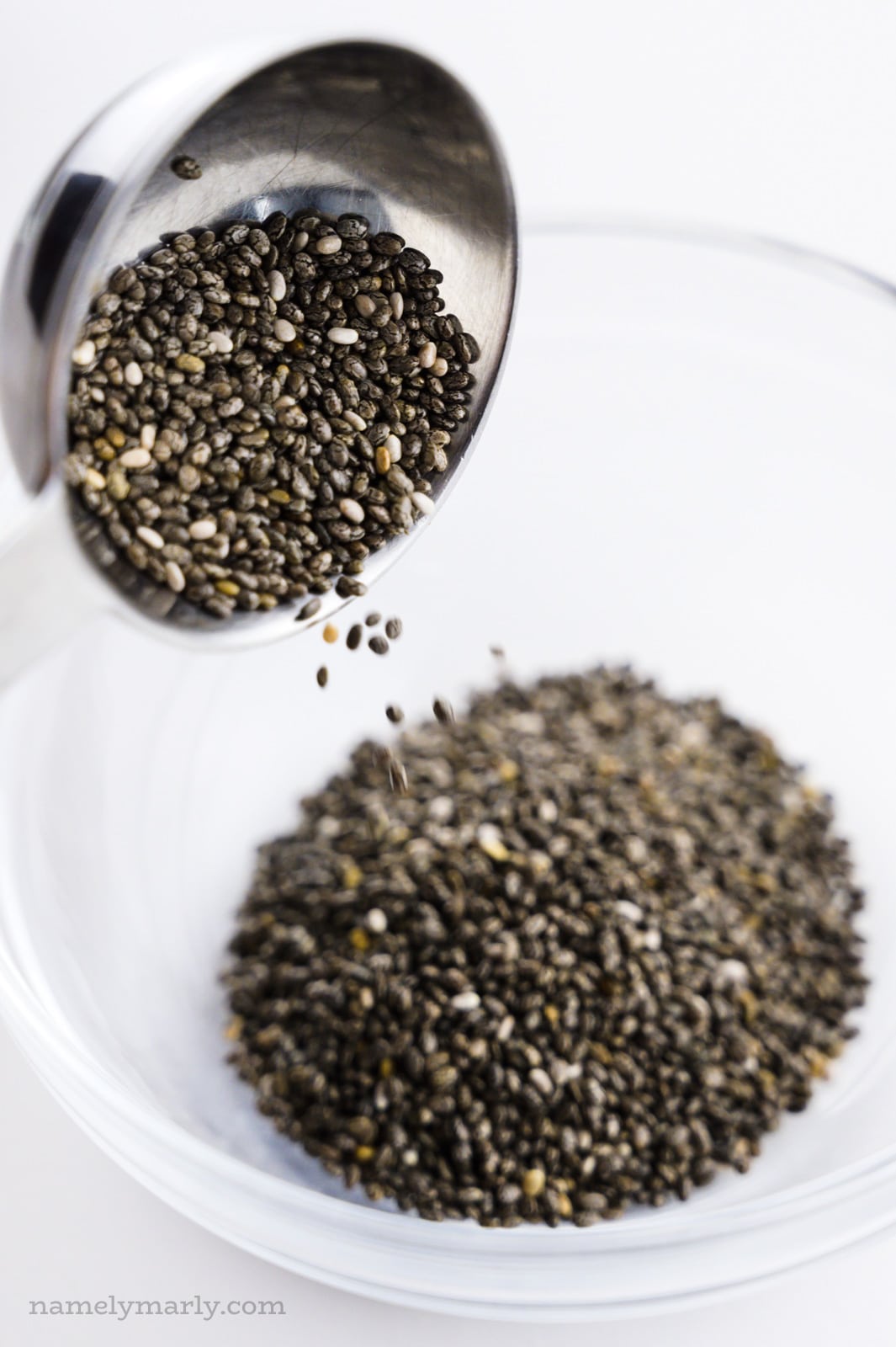 A tablespoon full of chia seeds is pouring them into a small glass bowl.
