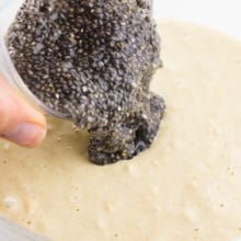A bowl full of wet chia seeds, referred to as a chia egg, is being poured into batter.