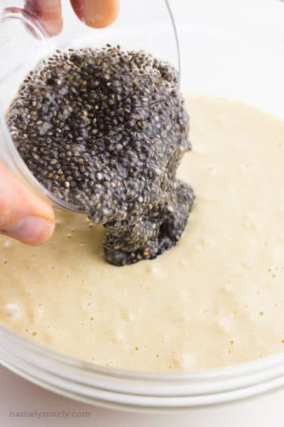 A bowl full of wet chia seeds, referred to as a chia egg, is being poured into batter.