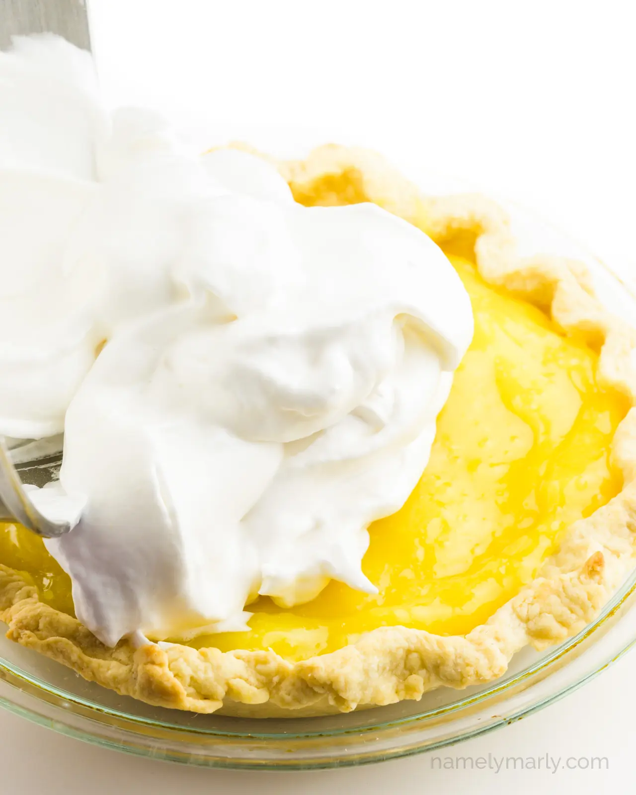 A bowl is pouring meringue over the top of a lemon pie.