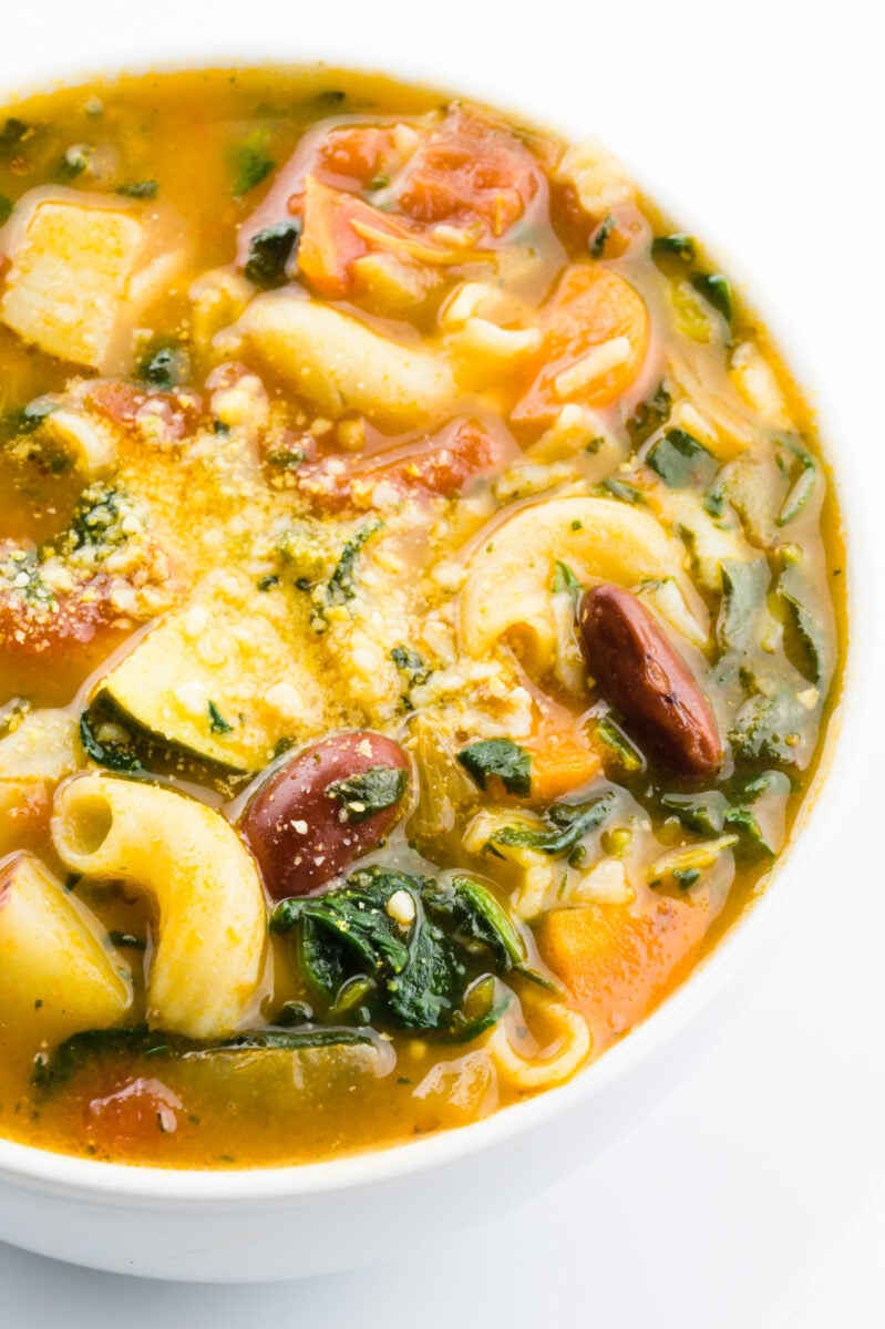 A closeup of a bowl of minestrone soup, showing noodles, beans, and other ingredients.