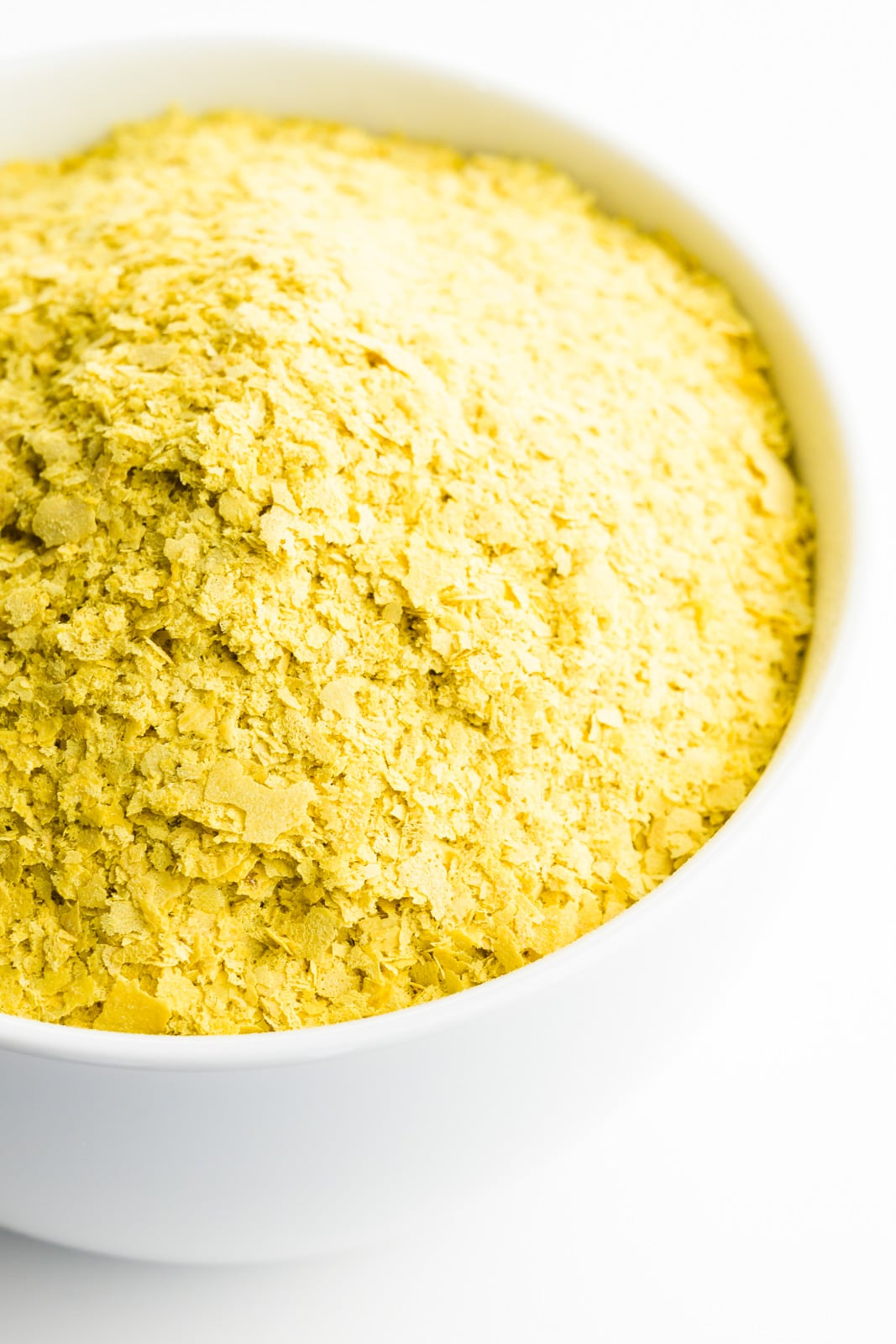 A bowl is full of yellow nutritional yeast flakes.