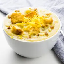 A bowl of vegan potato soup sits next to a grey cloth napkin.