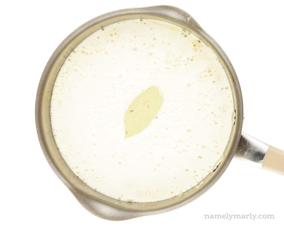 A saucepan holds chopped potatoes simmering in a cashew milk mixture. A bay leaf is on top.