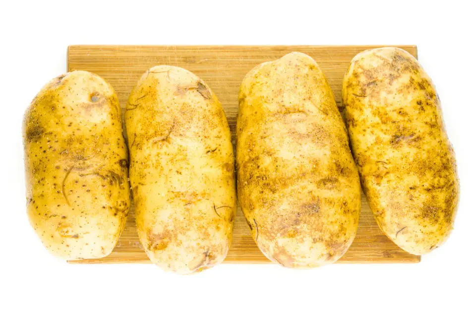 Four potatoes have been picked with a fork, covered with oil, and seasoned with salt and pepper. They are sitting on a cutting board.
