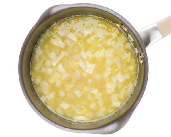 A saucepan is full of onions, broth, and other ingredients to make alfredo sauce.