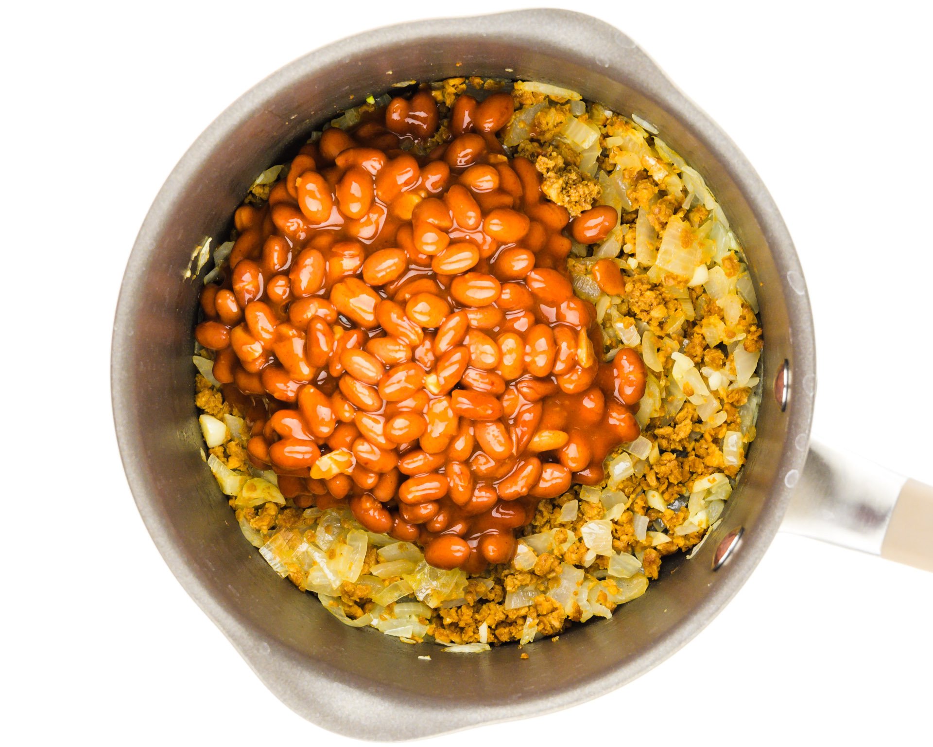 Beans have been added to a saucepan full of onions, garlic, and veggie crumbles.