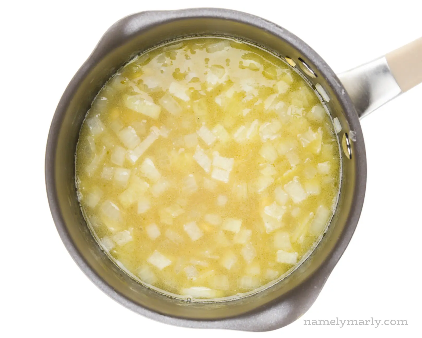 A saucepan is full of onions, broth, and other ingredients to make alfredo sauce.