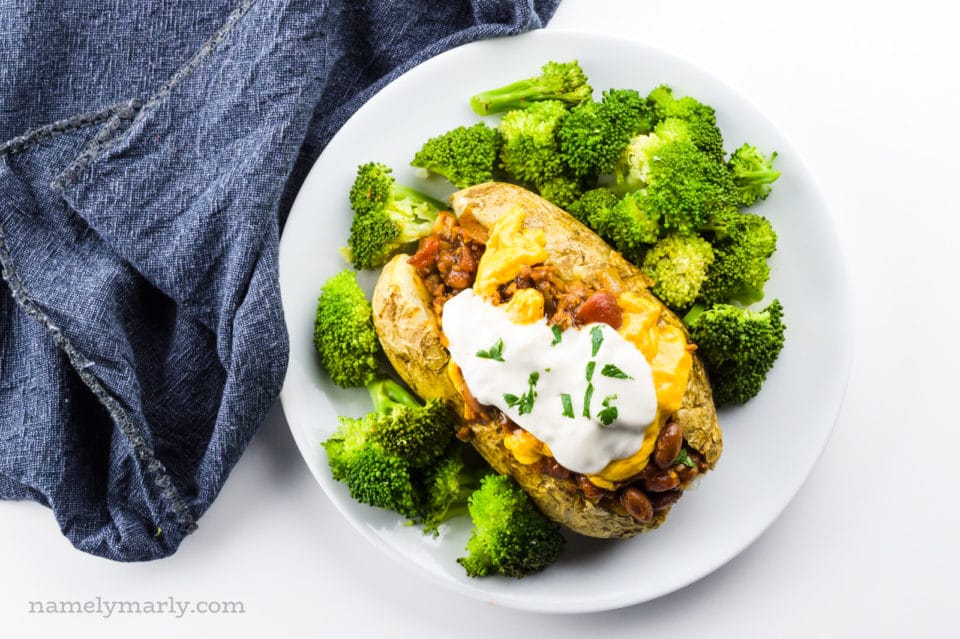 Looking down on a plate with a vegan baked potato with lots of toppings and steamed broccoli on the side.