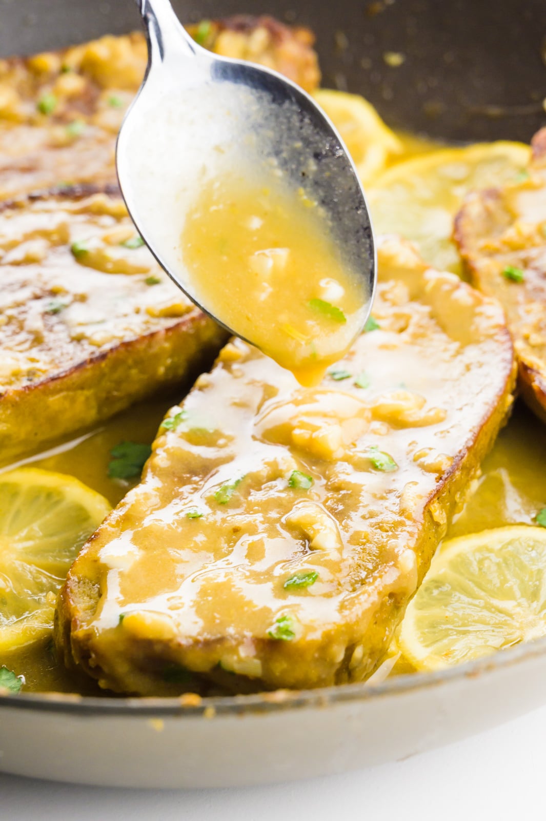 A spoon drizzles sauce over vegan chicken in a skillet.