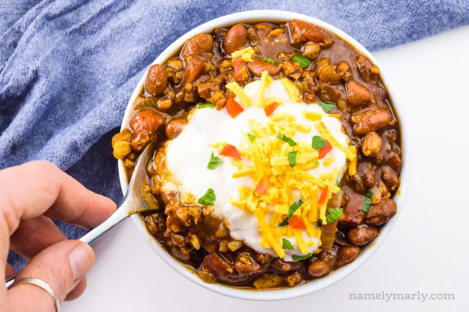 A hand holds a spoon dipping into a bowl of vegan chili.