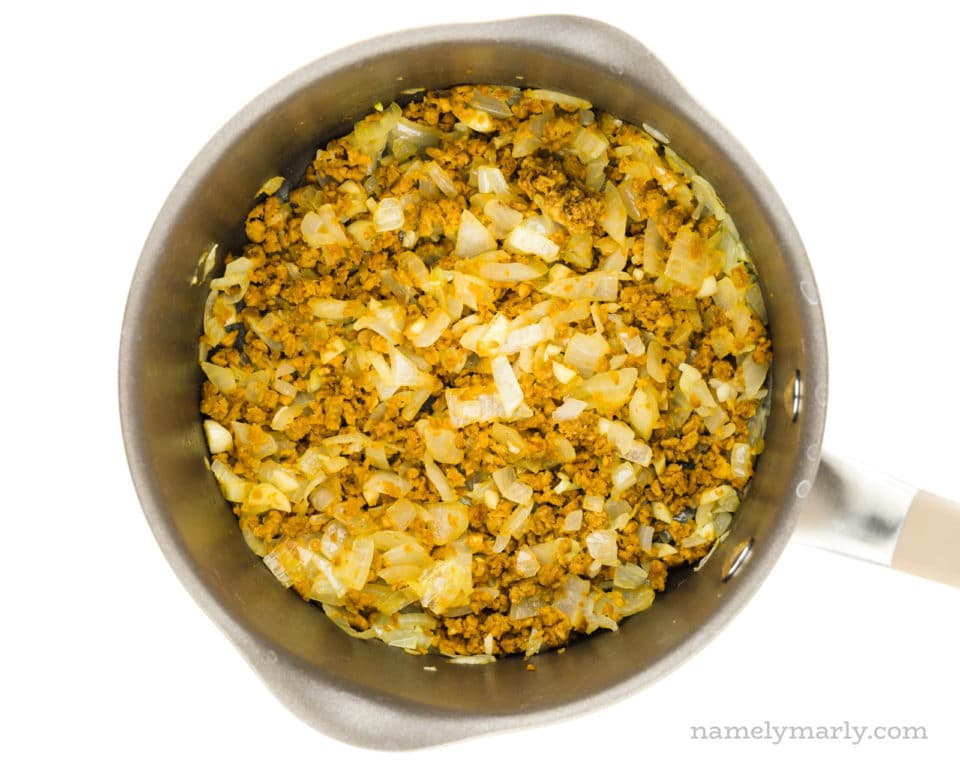 A saucepan holds onions, garlic, and veggie crumbles.