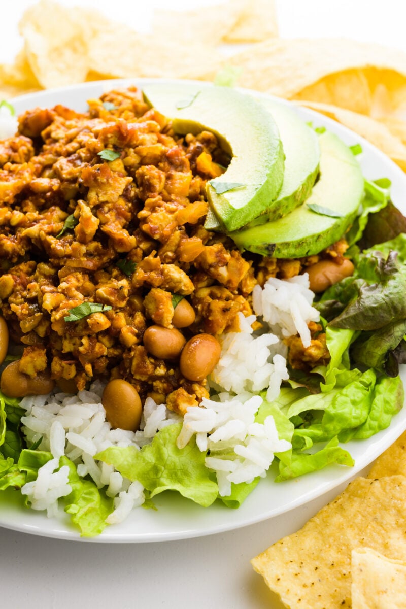 A plate with lettuce, rice, beans, and sofritas made from tofu is surrounded by tortilla chips.
