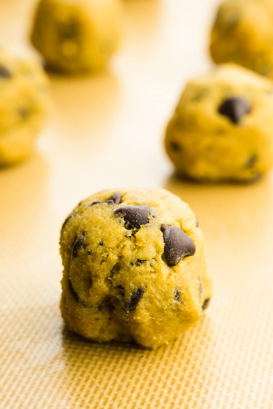 Chocolate chip cookie dough balls are lined up on a baking sheet ready to go into the oven.