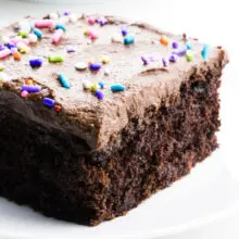 A slice of chocolate wacky cake has frosting and sprinkles on top.