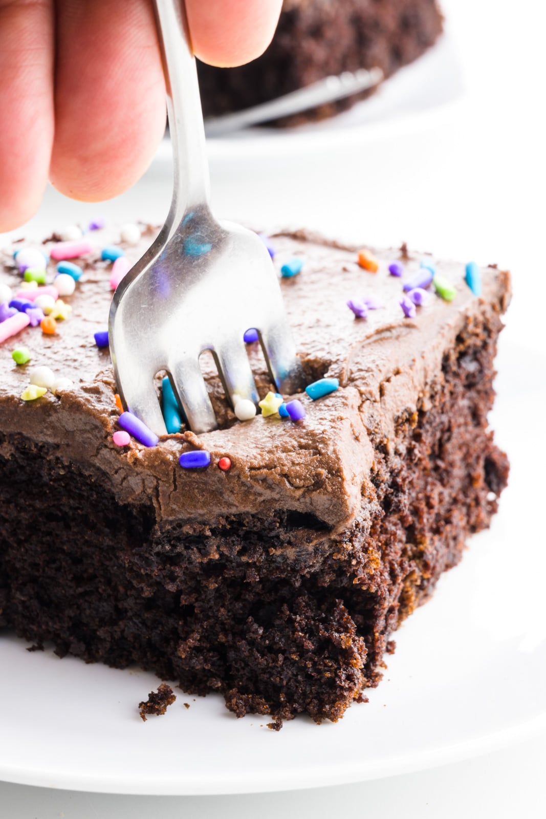 A hand holds a fork digging into a slice of chocolate cake.
