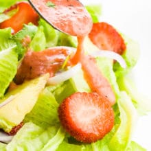 A spoon drizzles strawberry vinaigrette over a colorful green salad.