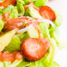 A closeup of a colorful green salad with pink dressing drizzled over the top.