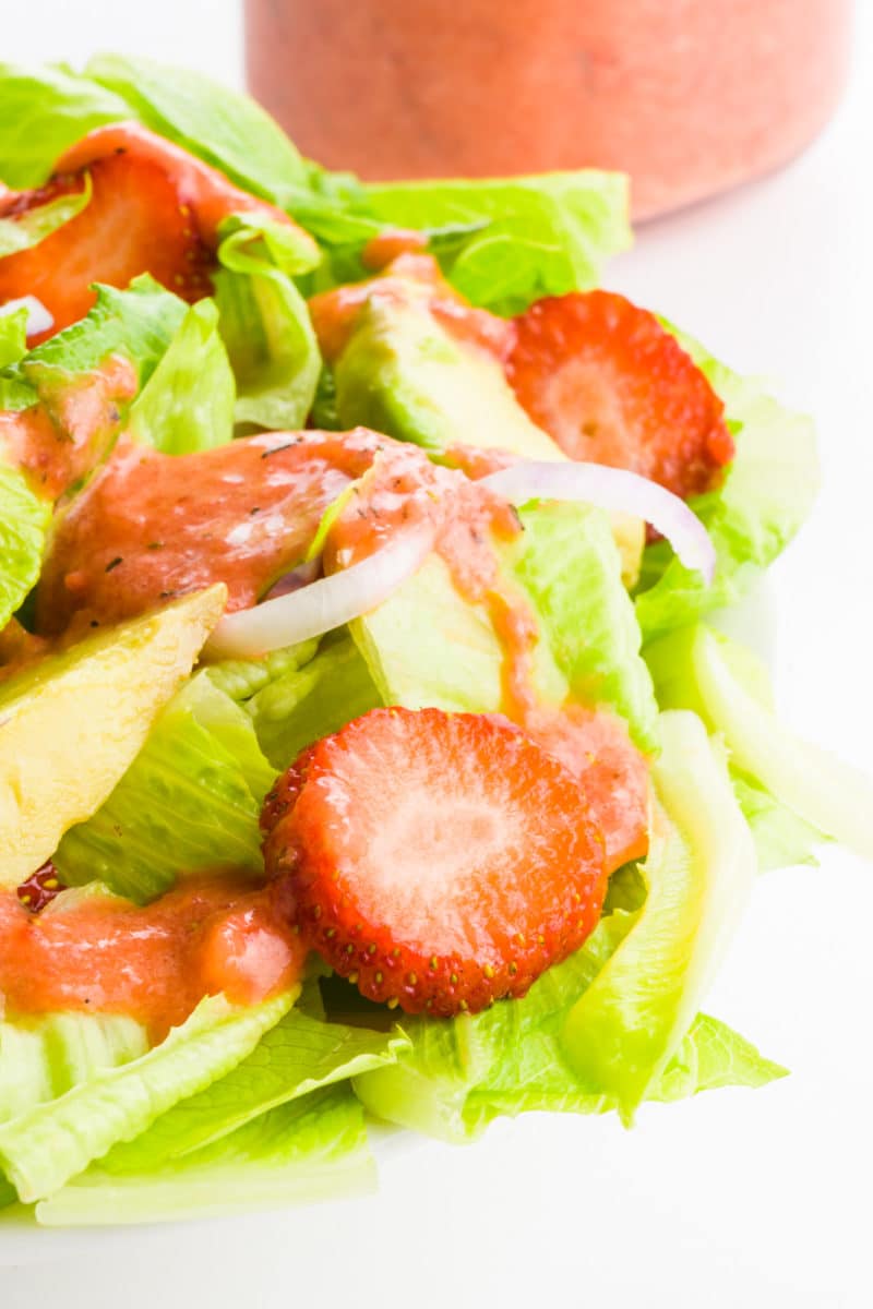A closeup of a colorful green salad with pink dressing drizzled over the top.