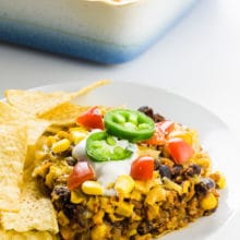 A plate holds a serving of vegan taco casserole with tortilla chips around it. The rest of the casserole is behind it.