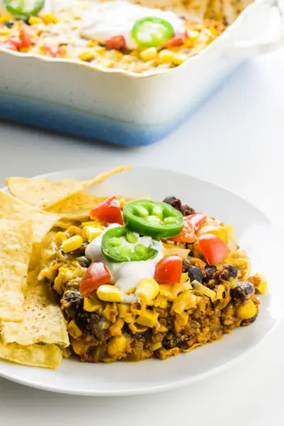 A plate holds a serving of vegan taco casserole with tortilla chips around it. The rest of the casserole is behind it.