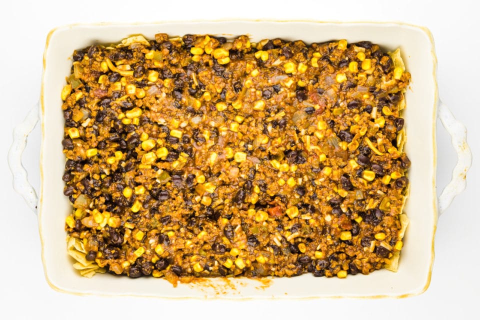 A bean mixture has been poured over crumbled tortilla chips in a casserole dish.