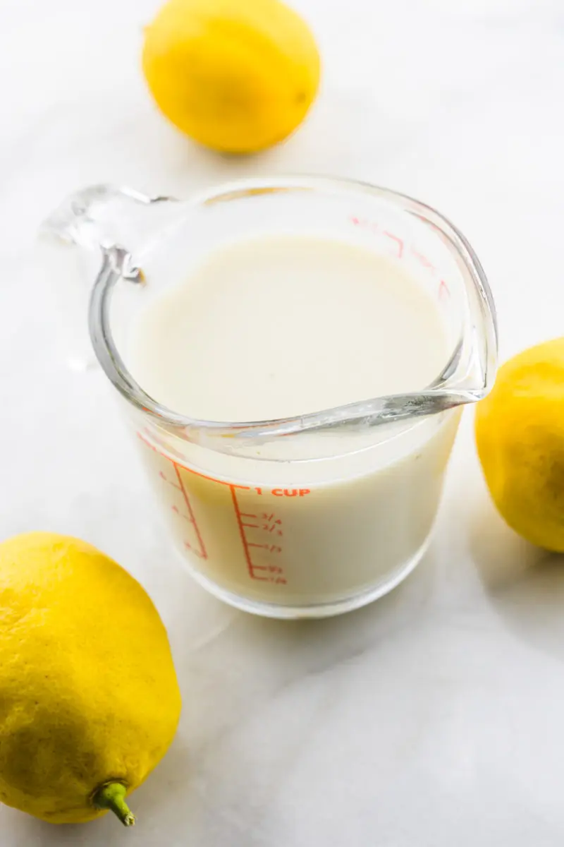 A measuring cup holds plant-based milk with 3 lemons around it.