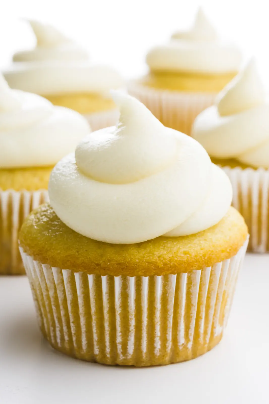 A vanilla cupcake has vanilla frosting swirled on top. there are several more cupcakes in the background.