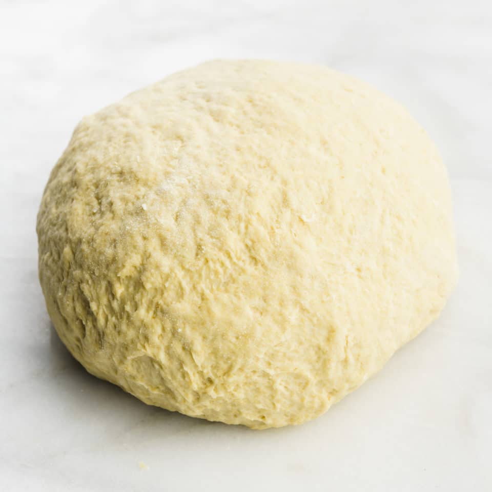 A ball of vegan pizza dough sits on a marbled countertop.