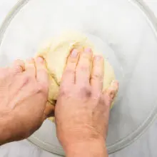 Two hands reach into a glass bowl, kneading some dough.