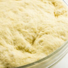 Dough has risen in a glass bowl and this photo shows how it now fills up the bowl to the edges.