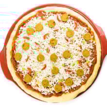 Looking down on an unbaked pizza on a red pizza stone.