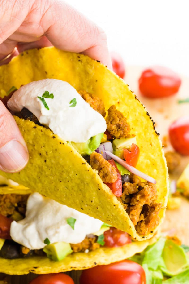 A hand holds a taco with vegan taco filling and cashew cream on top.