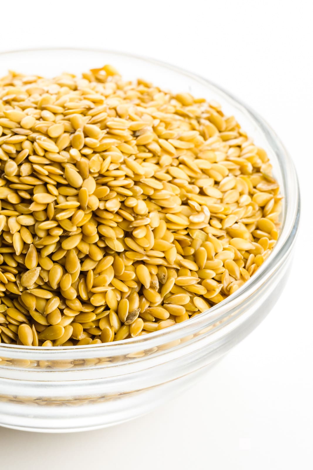 A bowl is full of whole golden flax seeds.