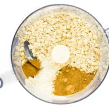 Oats and other ingredients are in the bottom of a food processor bowl.